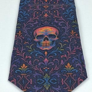 May include: A dark blue tie with a repeating floral pattern and a central skull motif. The skull and floral details are in orange, pink, purple, and blue. The tie has a pointed end and is set against a white backdrop.