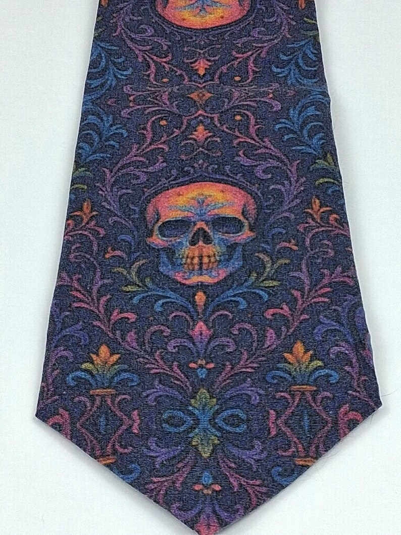 May include: A dark blue tie with a repeating floral pattern and a central skull motif. The skull and floral details are in orange, pink, purple, and blue. The tie has a pointed end and is set against a white backdrop.