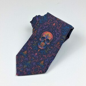 May include: A dark blue necktie with a colourful skull design. The tie features a repeating floral pattern in shades of purple, orange, and green. The skull is centered on the tie and is also multi-coloured.