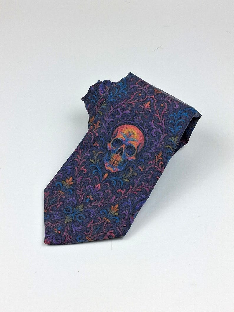 May include: A dark blue necktie with a colourful skull design. The tie features a repeating floral pattern in shades of purple, orange, and green. The skull is centered on the tie and is also multi-coloured.