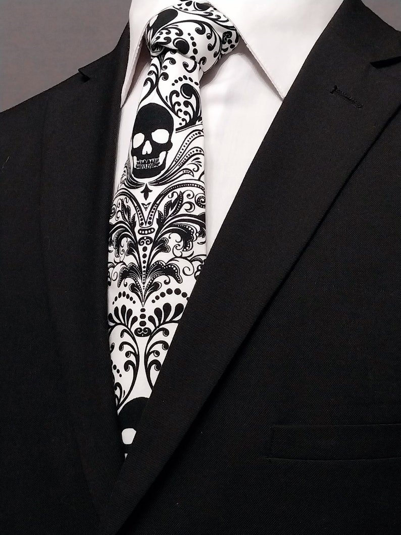 May include: A black suit jacket with a white dress shirt and a black and white tie featuring a skull and floral pattern.