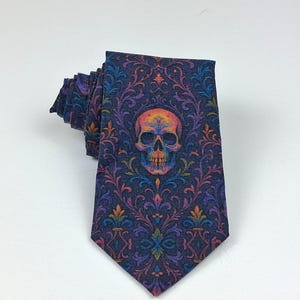May include: A dark blue tie featuring a repeating floral pattern and a central skull design. The skull is multi-coloured with orange, yellow, and purple hues. The tie is folded, displaying the intricate design.