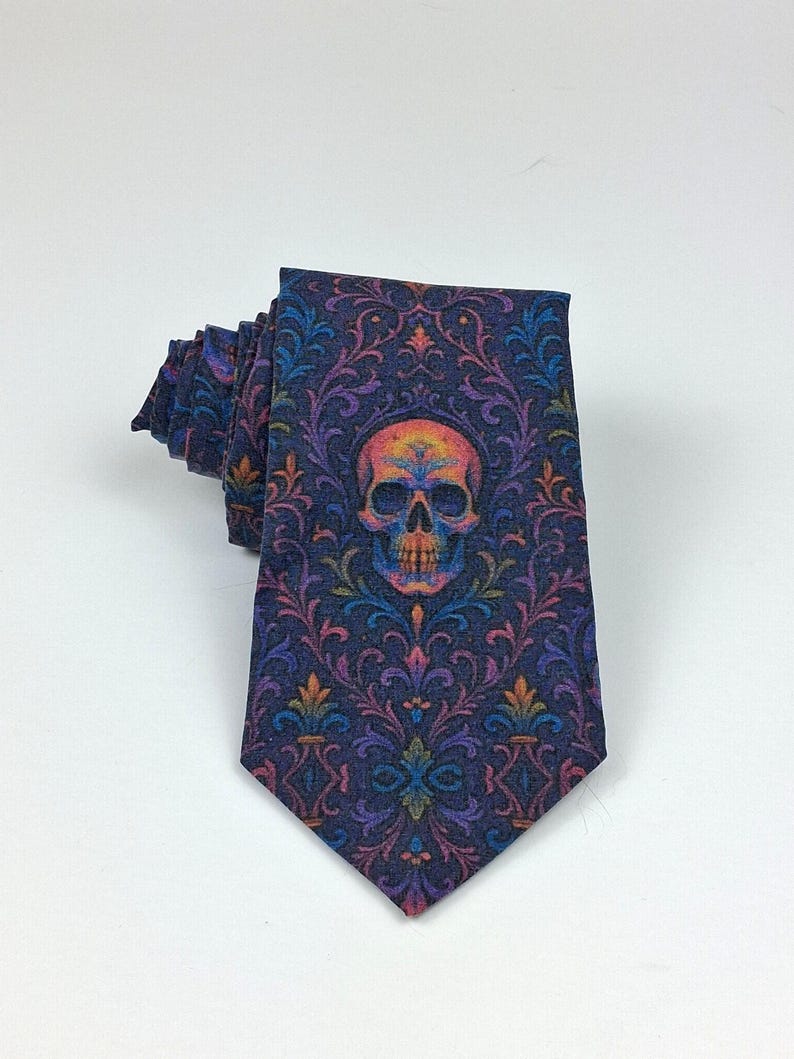 May include: A dark blue tie featuring a repeating floral pattern and a central skull design. The skull is multi-coloured with orange, yellow, and purple hues. The tie is folded, displaying the intricate design.