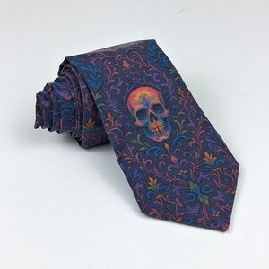 May include: A rolled-up necktie with a dark blue background and a colorful skull design. The skull is orange, yellow, and blue. The tie has a floral pattern in shades of blue, purple, and orange.