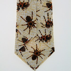 May include: A beige silk tie with a pattern of brown and orange spiders on a web design.
