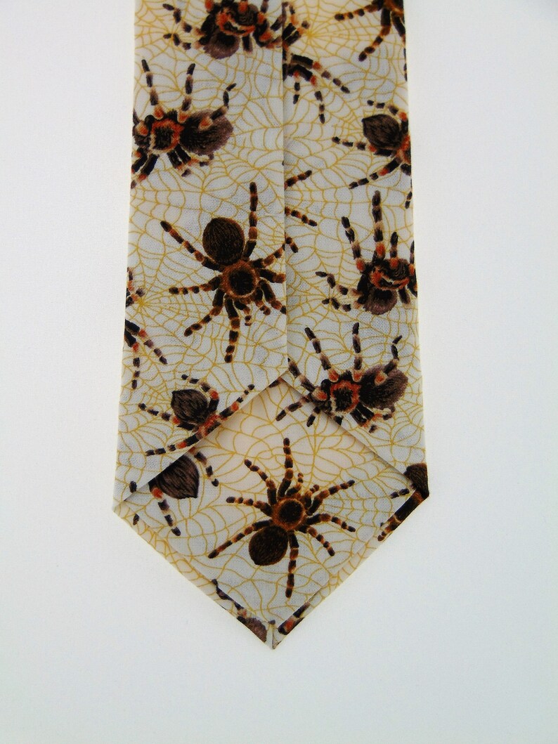 May include: A beige silk tie with a pattern of brown and orange spiders on a web design.