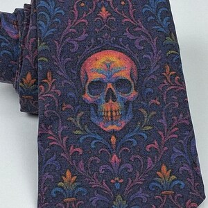 May include: A rolled-up tie featuring a dark blue backdrop and a vibrant skull motif. The skull is centrally positioned, encircled by a floral design in hues of purple, orange, blue, and green. The tie is crafted from a soft material.