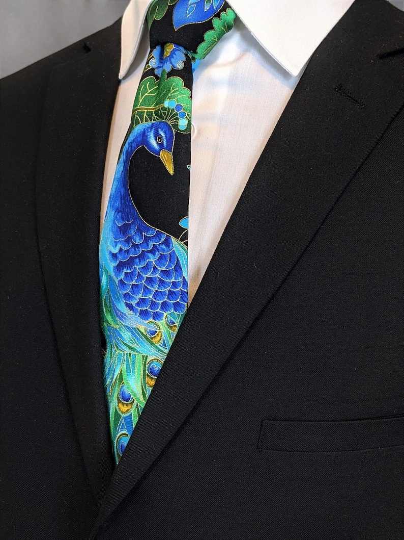 May include: A black suit jacket with a black and blue patterned tie featuring a peacock design. The tie has green, blue, and gold accents.