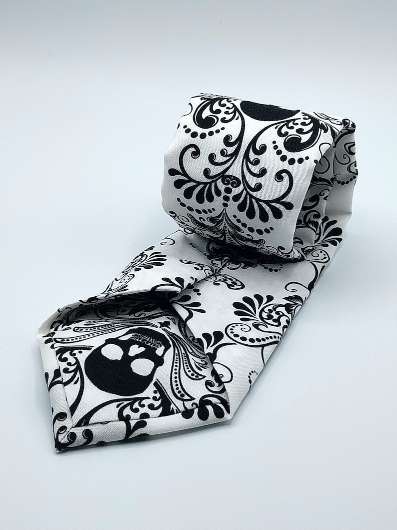 May include: A white tie with a black skull and floral pattern.