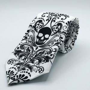 May include: A white tie with a black skull and floral pattern.