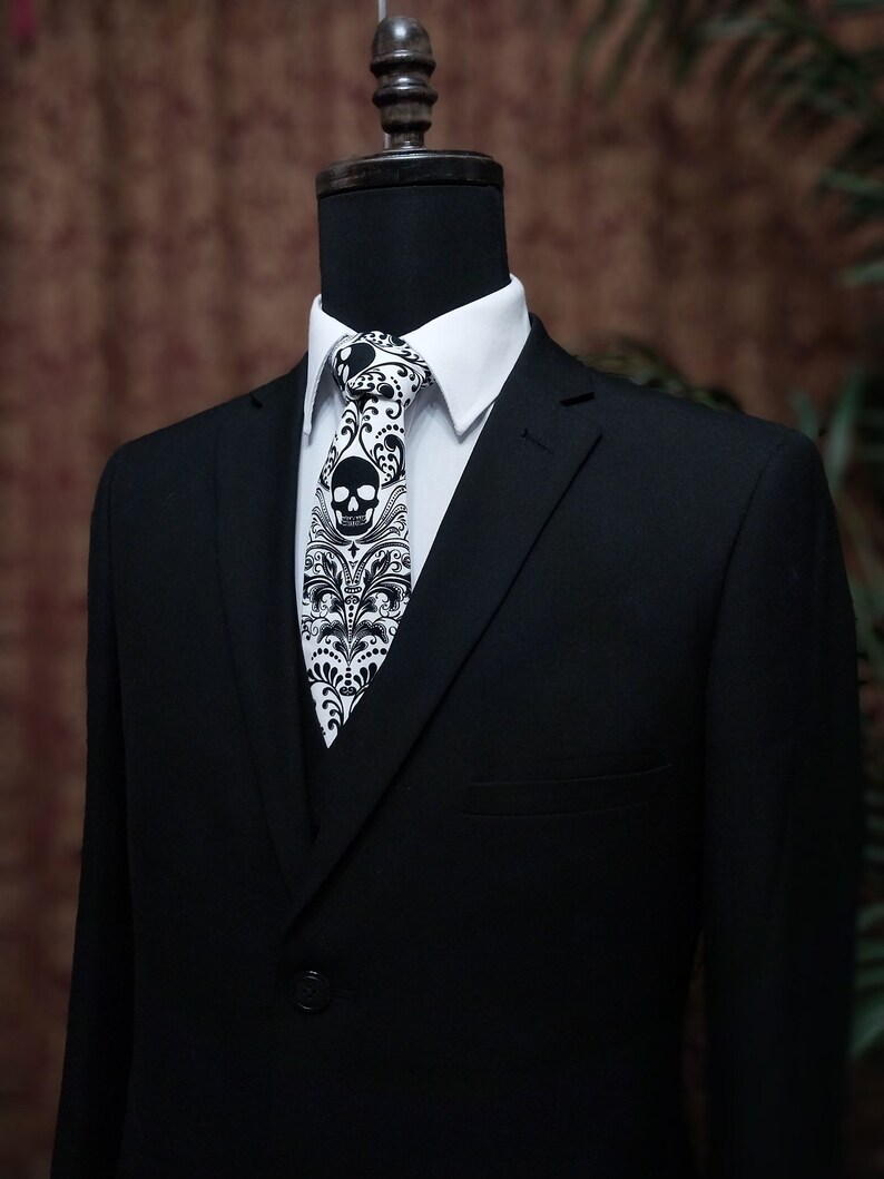 May include: A black suit jacket with a white collared shirt and a black and white skull patterned tie.