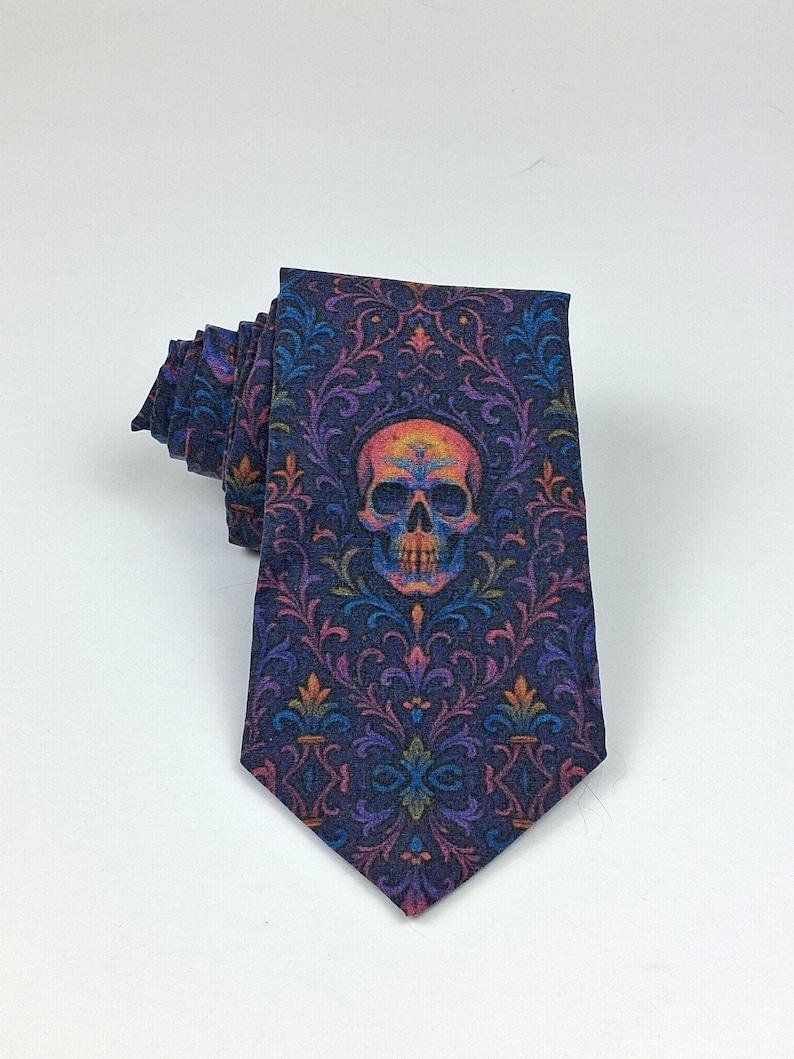 May include: A dark blue tie featuring a repeating floral pattern and a central skull motif. The skull is multi-coloured with orange, yellow, and purple shades. The tie is folded, displaying the detailed design.