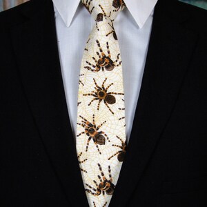 May include: A white tie with a pattern of brown tarantulas and yellow spiderwebs.