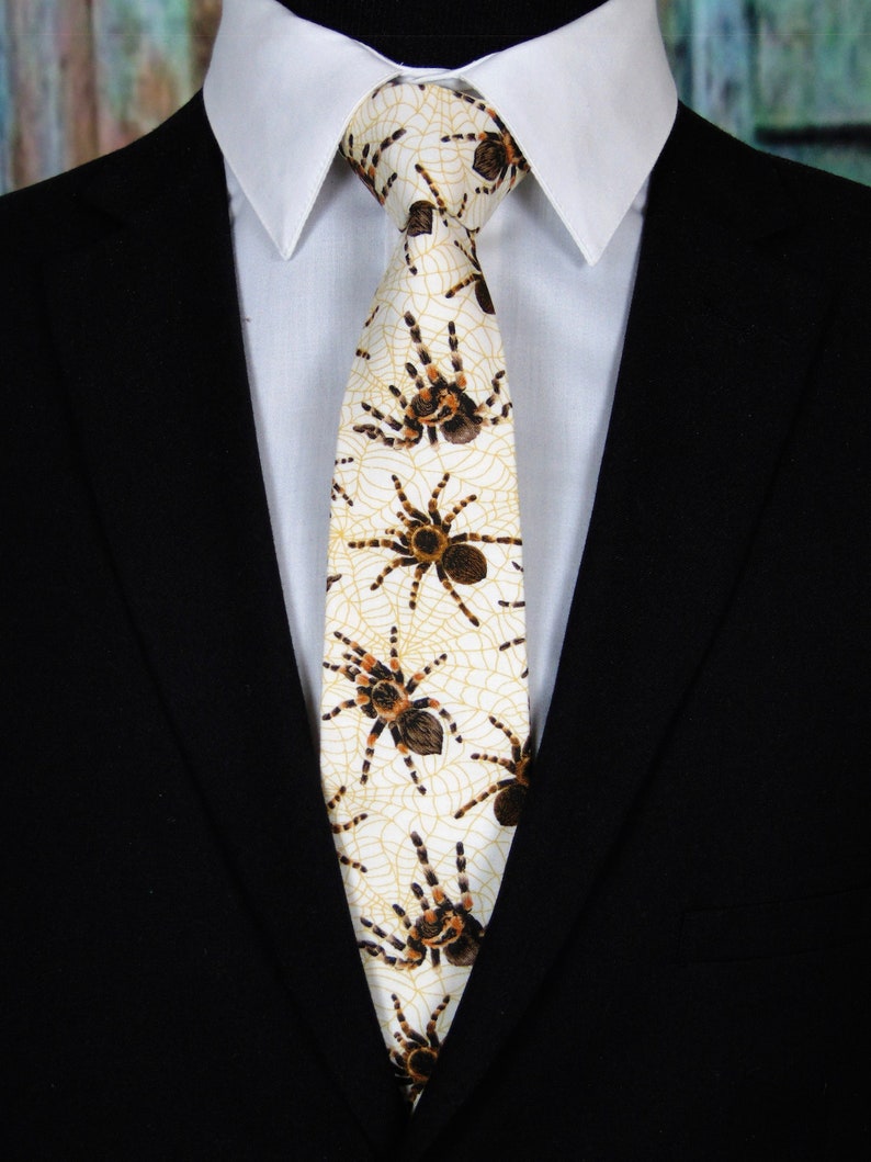 May include: A white tie with a pattern of brown tarantulas and yellow spiderwebs.