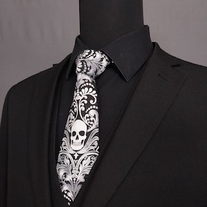 May include: A black suit with a white skull and floral patterned tie. The tie has a silver and black design.