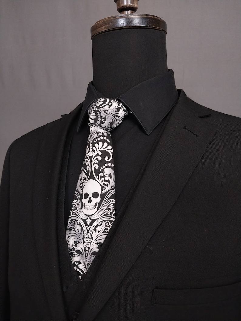 May include: A black suit with a white skull and floral patterned tie. The tie has a silver and black design.