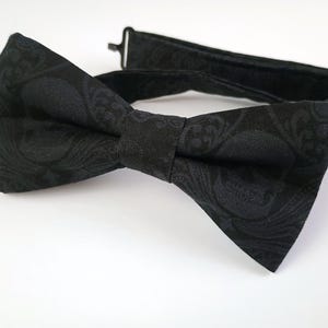 May include: A black bow tie with a paisley pattern. The bow tie is made of a soft, textured fabric.