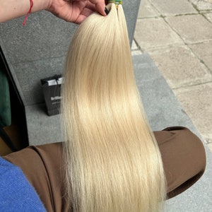 May include: A long, straight, blonde hair extension with a light, golden hue. The hair is held together with rubber bands.