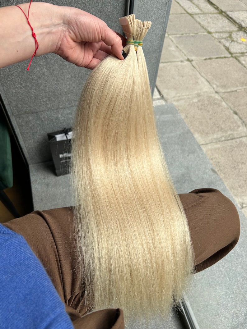 May include: A long, straight, blonde hair extension with a light, golden hue. The hair is held together with rubber bands.