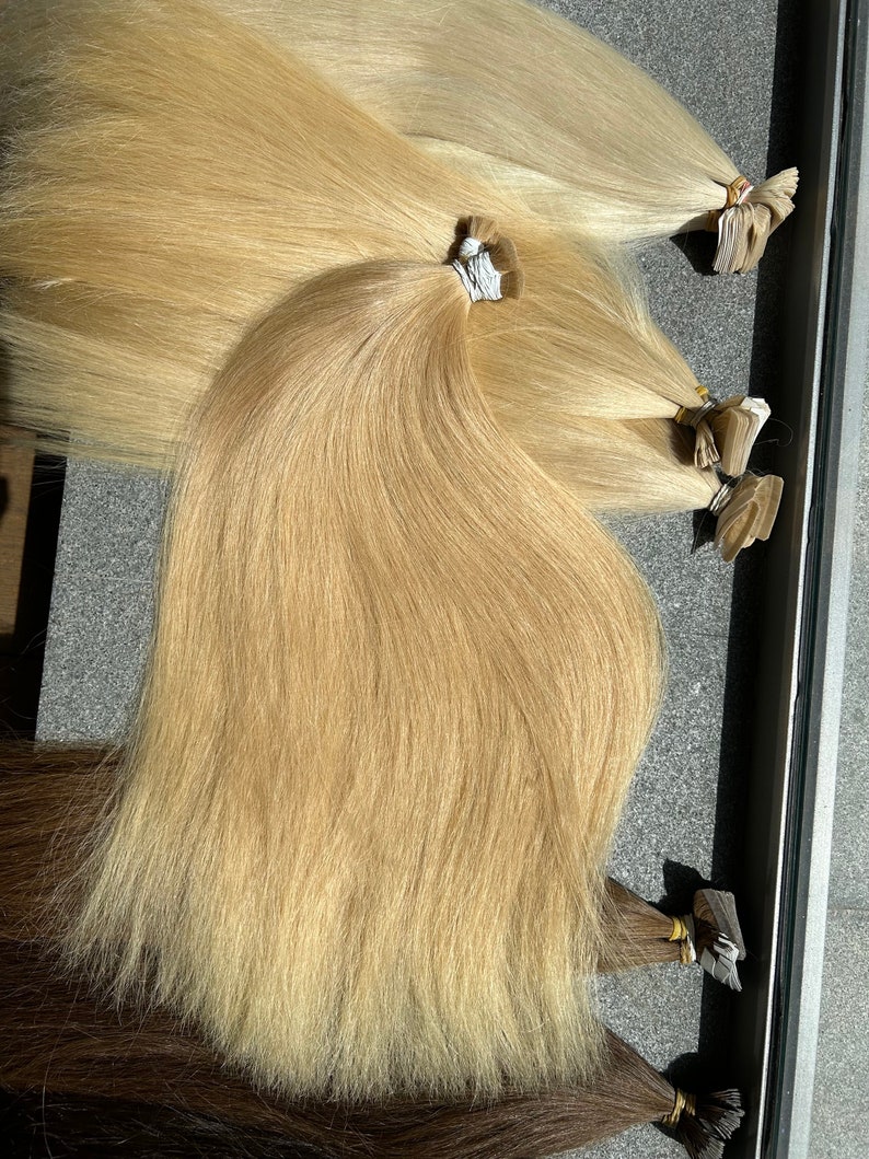 May include: Multiple strands of light blonde human hair extensions. The hair is straight and appears to be very long. The extensions are attached to wefts with a clear adhesive tape.