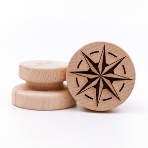 Könnte beinhalten: Zwei Holzgriffe mit einem Sternmuster. Der obere Griff hat ein Kompassrosenmuster mit einem Stern in der Mitte. Der untere Griff ist schlicht.