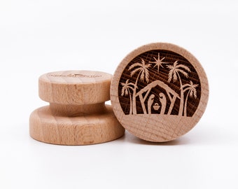 May include: Two wooden bottle stoppers. One stopper features a detailed laser-etched Nativity scene with palm trees, a star, and a manger. The other stopper has the text "special creations" etched on the top. Both stoppers are made of light-colored wood.