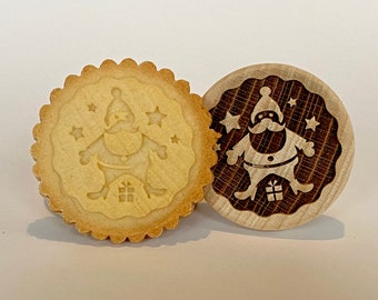 May include: A wooden cookie cutter and a cookie with a raised design of a Santa Claus holding a gift. The cookie cutter is made of wood and has a brown finish. The cookie is light brown and has a slightly crispy texture.