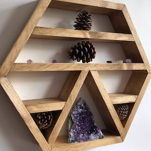 May include: A hexagonal wooden shelf with multiple shelves and compartments, featuring a large amethyst crystal, pine cones, and small purple crystals.
