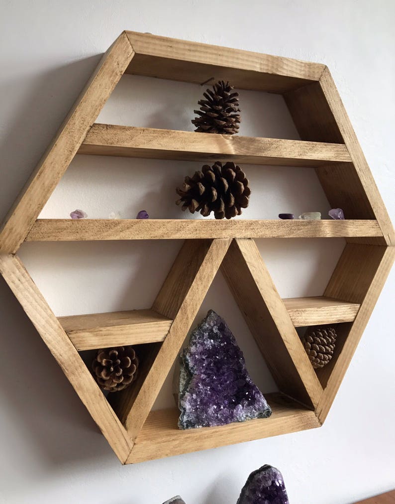 May include: A hexagonal wooden shelf with multiple shelves and compartments, featuring a large amethyst crystal, pine cones, and small purple crystals.