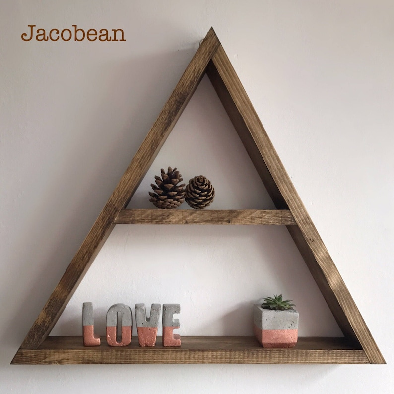 Puede incluir: Estanter&iacute;a triangular de madera con dos niveles. Contiene dos pi&ntilde;as, la palabra "LOVE" en letras grises y coral, y una peque&ntilde;a suculenta en maceta. La estanter&iacute;a es de color marr&oacute;n c&aacute;lido y est&aacute; montada en una pared blanca.