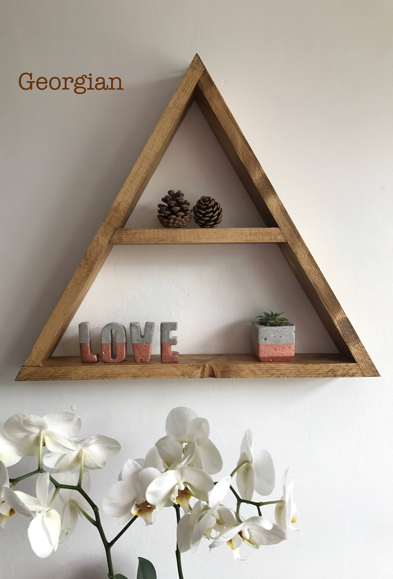 Puede incluir: Estanter&iacute;a triangular de madera con dos niveles, que contiene dos pi&ntilde;as, letras de hormig&oacute;n que deletrean "LOVE" con un acento coral y una peque&ntilde;a suculenta en maceta. La palabra "Georgian" es visible.