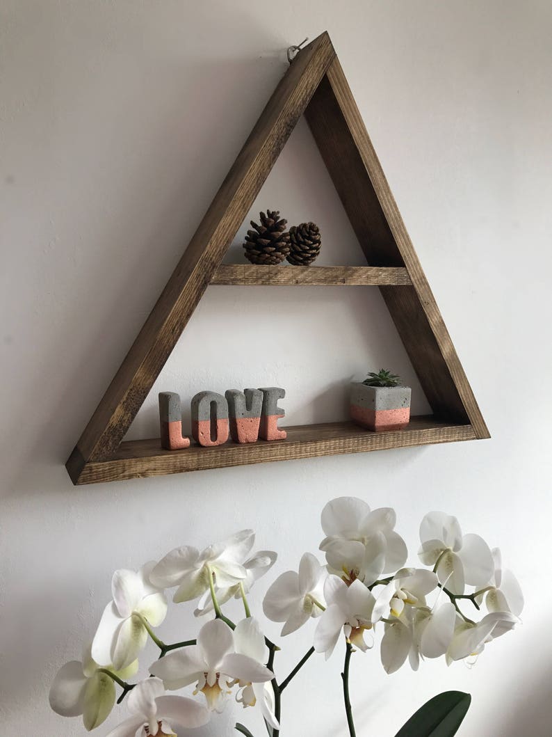 Puede incluir: Una estanter&iacute;a triangular de madera marr&oacute;n con dos niveles. La balda superior contiene dos pi&ntilde;as. La balda inferior muestra una escultura de hormig&oacute;n con la palabra "LOVE" en gris y coral, y una peque&ntilde;a planta en maceta.