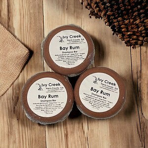 May include: Three brown shampoo bars with white labels that read "Ivy Creek Harris County, GA IvyCreekGardens.com Ivy Creek Gardens etsy.com Bay Rum Shampoo Bar Natural pH 5.0-6.0 Soap Free Vegan Suitable for Sensitive Skin/Scalp Ingredients: Sodium Cocoate, Water, Glyceryl Stearate, Propylene Glycol, Moroccan Clay, Fragrance Oil 1 bar (3 oz)"