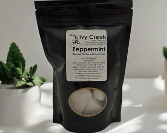 May include: A black resealable bag with a clear window showing white peppermint shower fizzies. The bag has a label that reads "Ivy Creek Peppermint Shower Fizzies with Menthol".