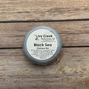 May include: A gray round bar of soap with the text "Ivy Creek Harris County, GA Ivycreekgardens.com IvyCreekGardens etsy.com Black Sea Shampoo Bar Natrural pH 5.0-6.0 Soap Free Vegan Suitable for Sensitive Skin/Scalp Ingredients: Sodium Cocoyl Isethionate Propylene Glycol Glyceryl Stearate Glyce Water Activated Charcoal Fragrance Oil 1 bar (3 oz)" printed on it.