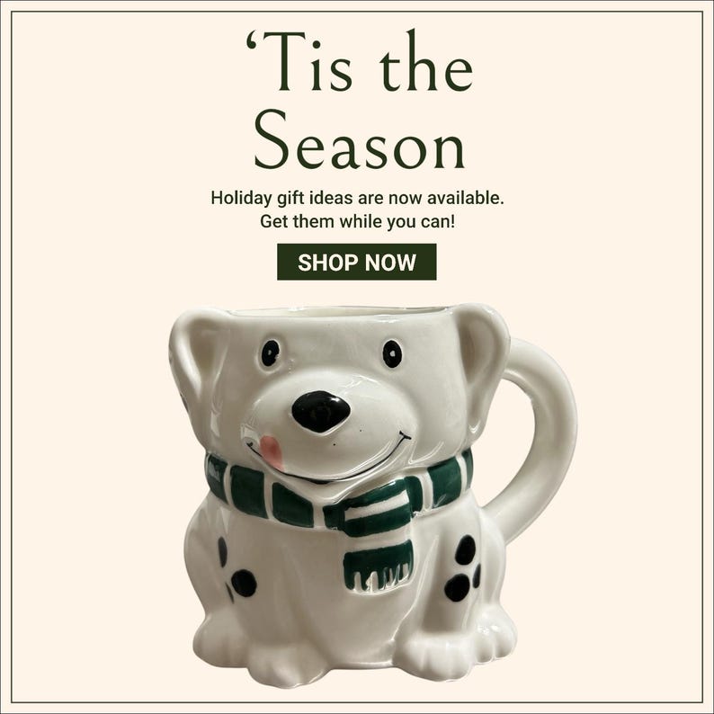 May include: White ceramic mug shaped like a dog wearing a green and white scarf. The mug has black spots and a pink tongue sticking out. 'Tis the Season' text is above the mug.  Holiday gift ideas are now available. Get them while you can! SHOP NOW