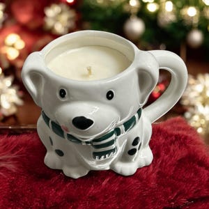 May include: White ceramic candle holder shaped like a dog wearing a green scarf. The candle is white and has a wick.