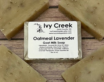 May include: Four bars of oatmeal lavender goat milk soap arranged around a central label. The label reads "Ivy Creek" and "Oatmeal Lavender Goat Milk Soap." Each bar is a light beige color and contains visible oatmeal flakes. The label also lists the ingredients.