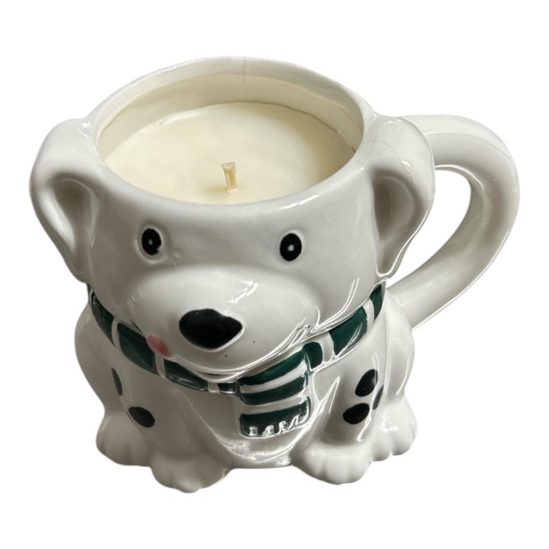 May include: White ceramic candle holder shaped like a dog wearing a green and white scarf. The candle is white and has a wick.