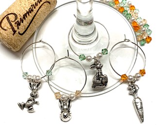 May include: Set of four Easter-themed wine glass charms. Each charm features a silver bunny rabbit with different poses and a crystal bead and pearl embellishment. The charms are attached to silver rings.