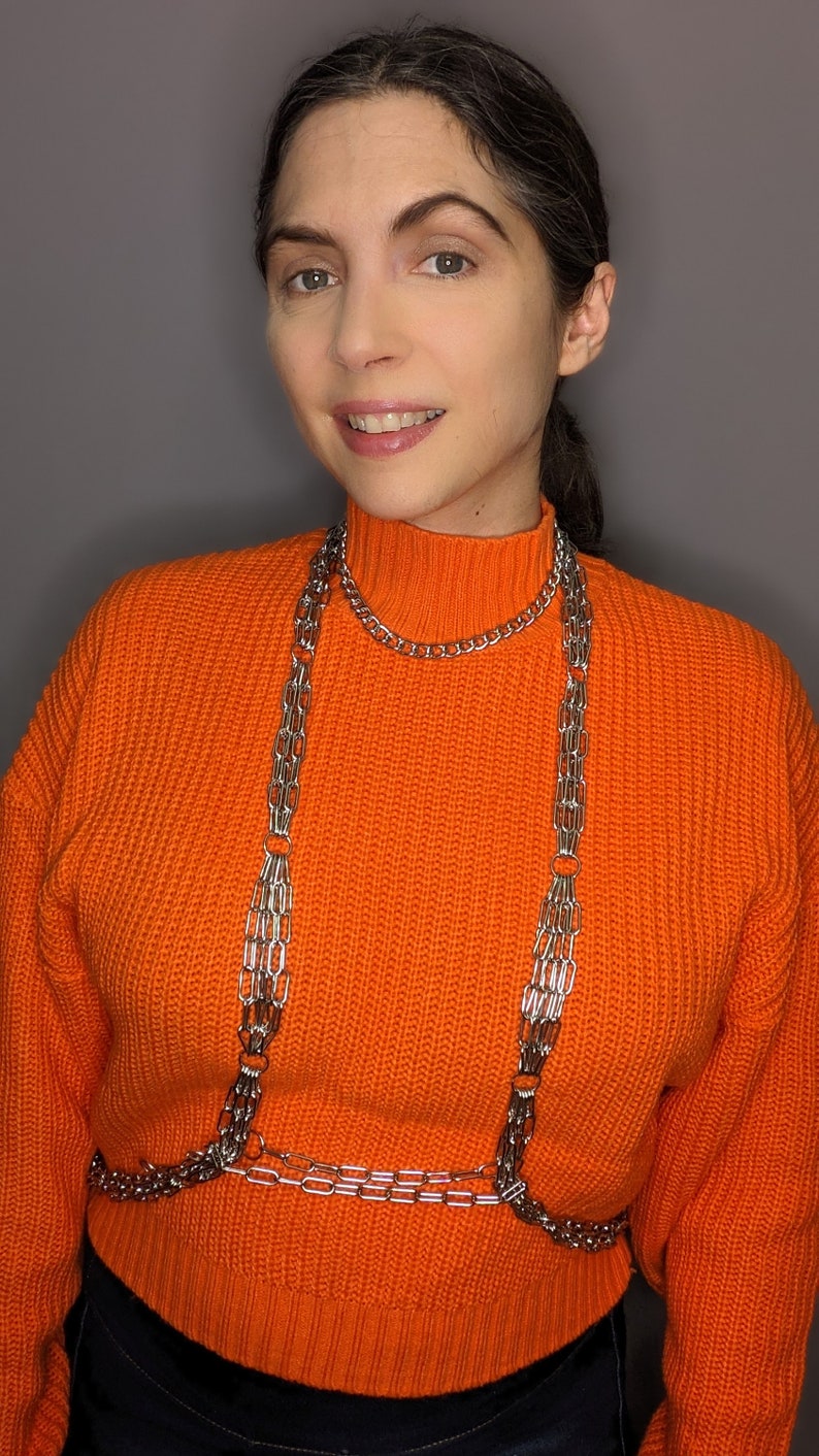 May include: A woman wearing an orange jumper with a silver chain body harness.