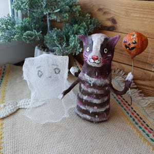 May include: A handmade Halloween decoration featuring a striped cat holding a pumpkin-shaped balloon and a white ghost with a tail.