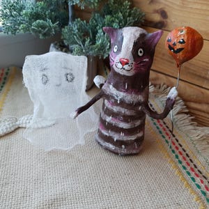 May include: A handmade Halloween decoration featuring a striped cat holding a jack-o'-lantern balloon and a white ghost with a tail.