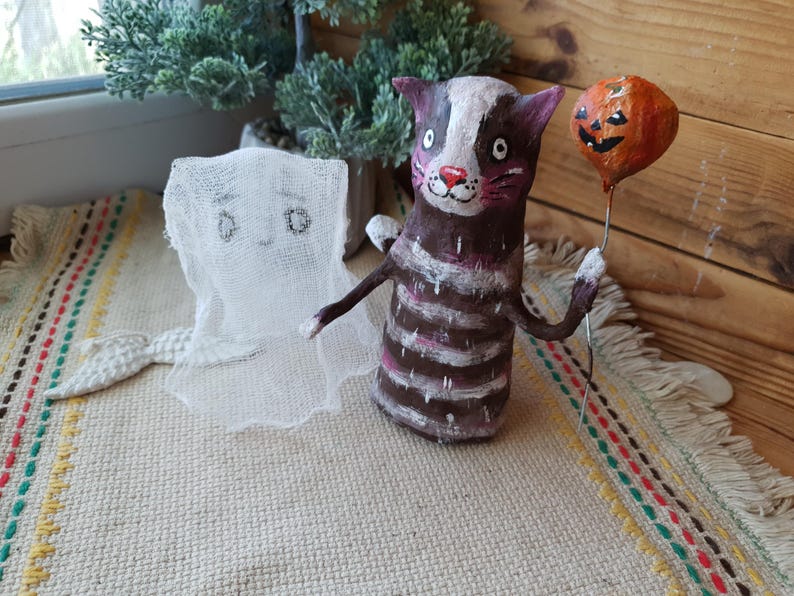 May include: A handmade Halloween decoration featuring a striped cat holding a jack-o'-lantern balloon and a white ghost with a tail.