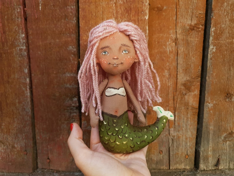 May include: A handmade doll with pink yarn hair, a green mermaid tail, and a white top. The doll has a painted face with brown skin, blue eyes, and freckles.