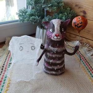 May include: A handmade Halloween decoration featuring a striped cat holding a pumpkin balloon and a ghost with a white fabric body.