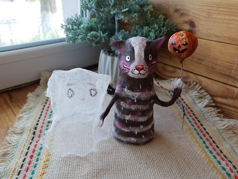 May include: A handmade Halloween decoration featuring a striped cat holding a pumpkin balloon and a ghost with a white fabric body.