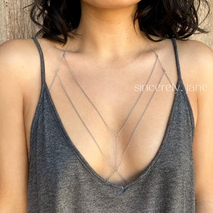 A woman wearing a stylish handmade silver stainless steel chain bra body chain, layered beneath a low-cut gray tank top. The gold body chain features a double layered chain arrangement across the chest. Brand is Sincerely, Jane