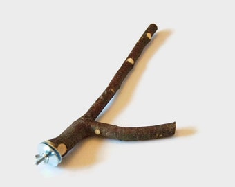 Pode incluir: Poleiro de madeira natural para pássaros com design de galho. O poleiro é marrom com pequenas manchas brancas e ferragens de metal. Projetado para ser fixado a uma gaiola de pássaros.