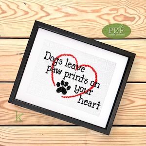 May include: A framed cross-stitch design with a red heart and paw print. The text reads "Dogs leave paw prints on your heart."